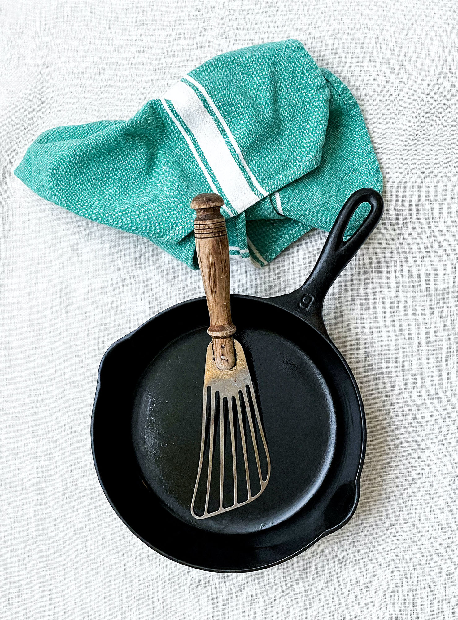 A green dish rag above a cast iron skillet with metal spatual in it. The image was obtained from Unsplash at https://unsplash.com/photos/FUsq49lD1xY